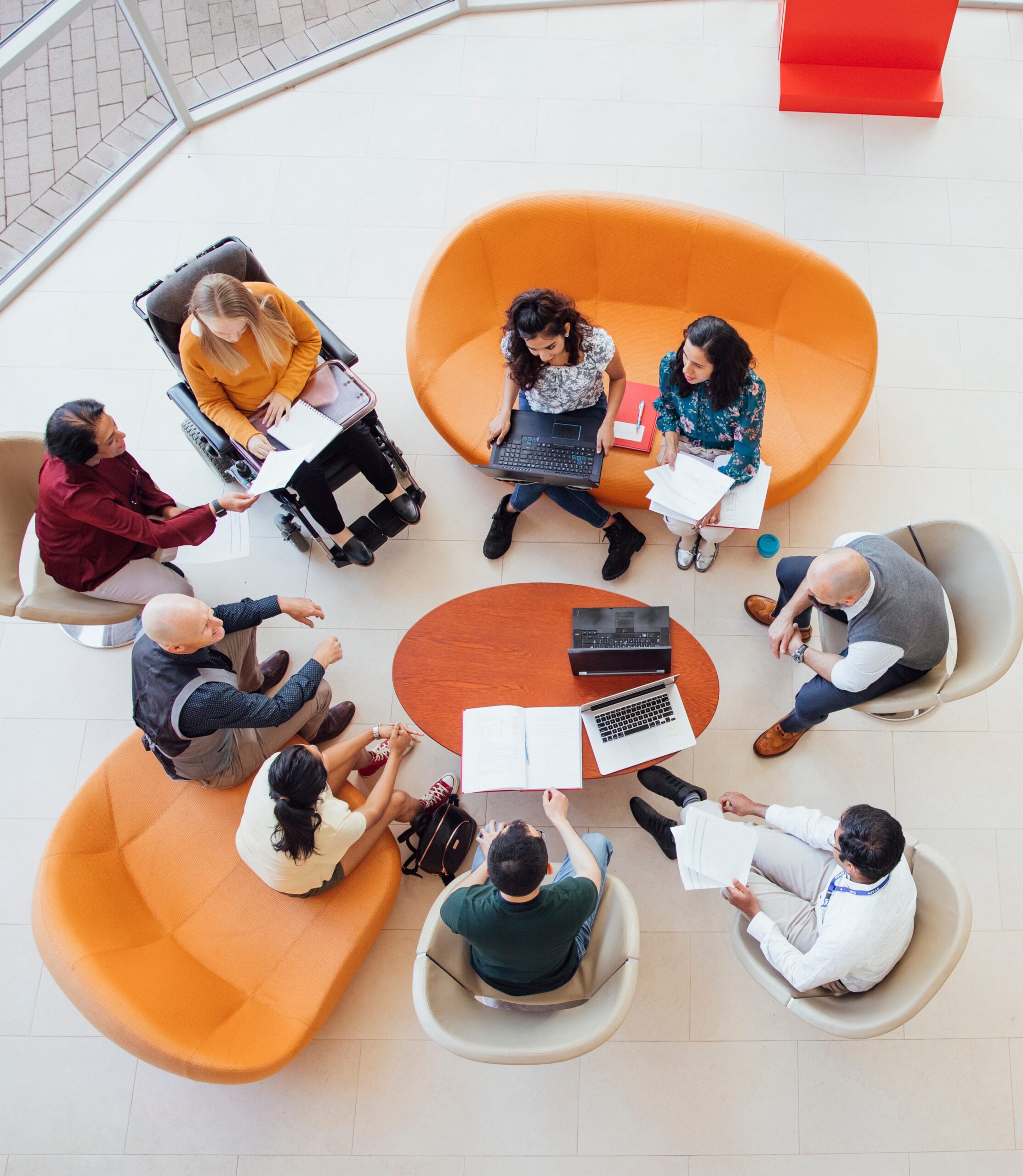 A top-down view of a diverse team, including a person in a wheelchair, having a meeting in a modern lounge area.