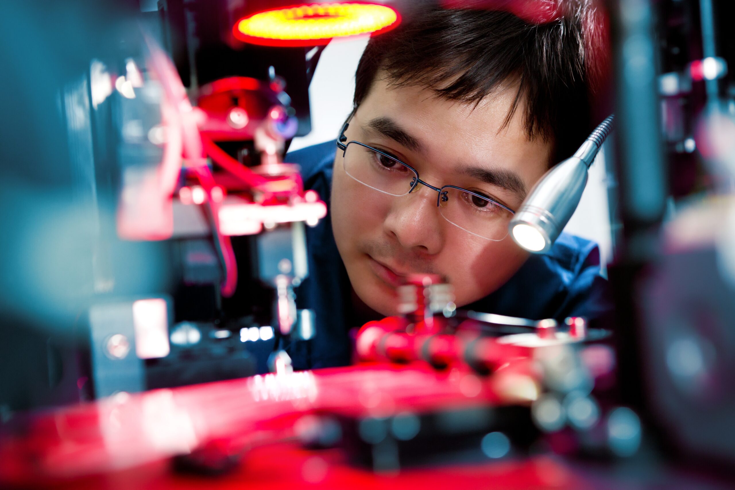 A focused technician working on a piece of advanced equipment. Bright lights and intricate machinery surround the workspace.