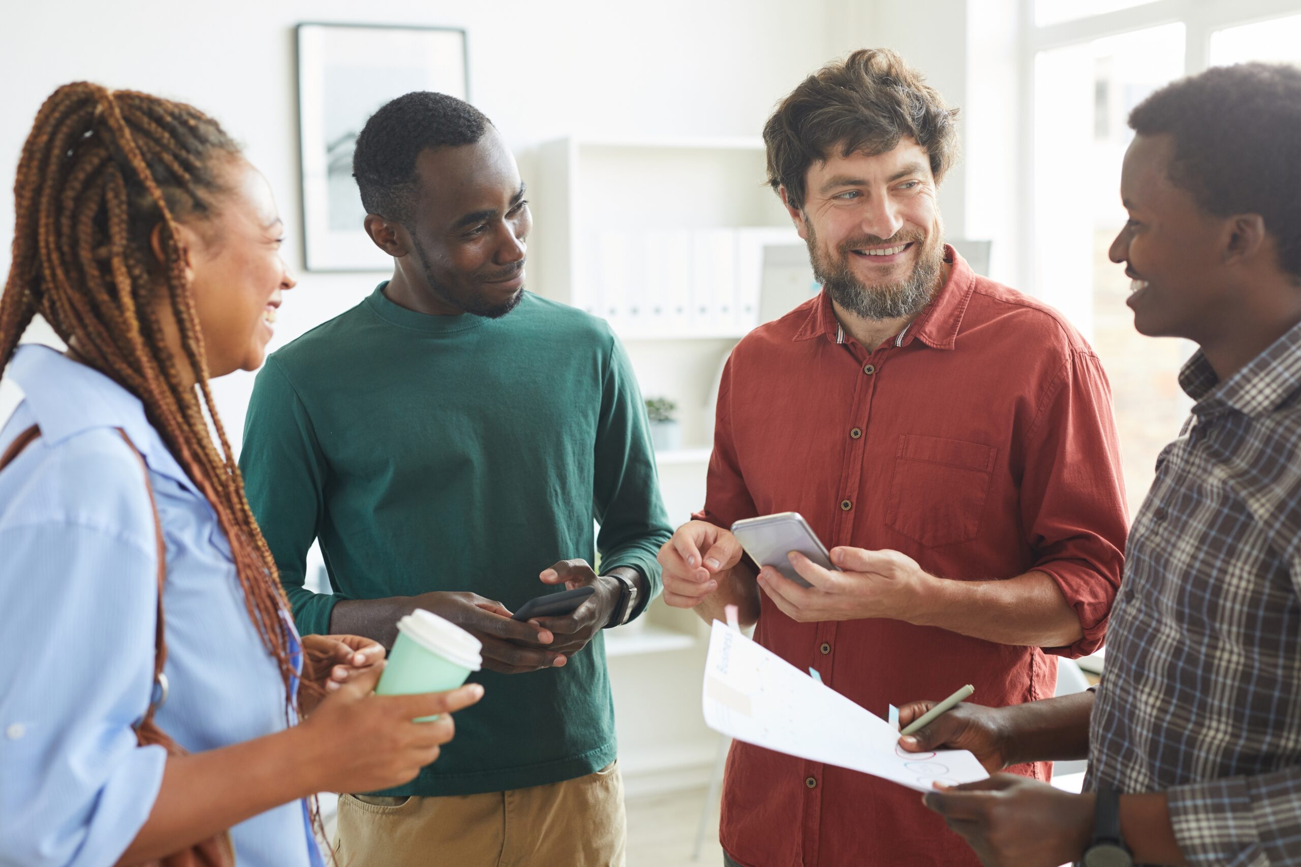 A small group of coworkers in an office laughing and chatting while sharing documents.