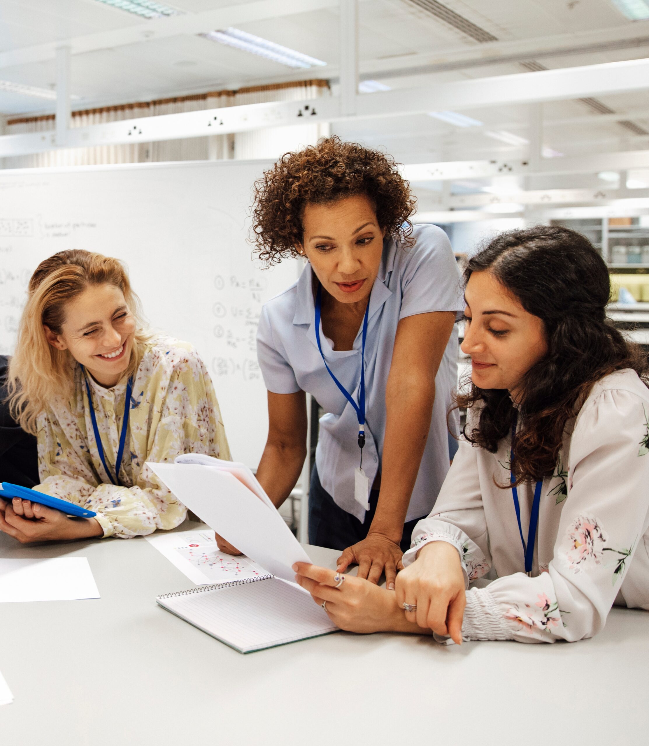 Three female colleagues in a meeting, discussing documents at a table in a bright, modern workspace.