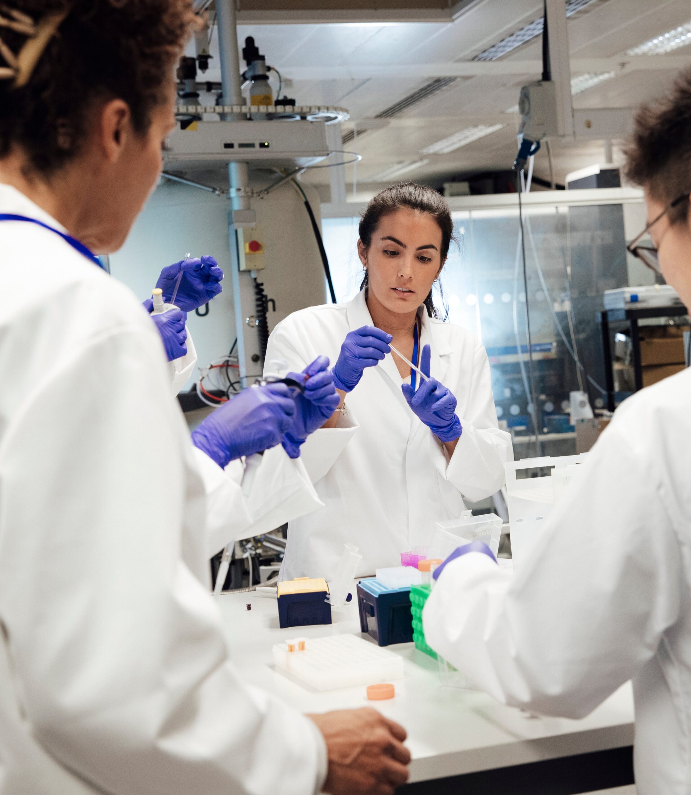 A group of lab workers in white coats and gloves collaborating on an experiment in a laboratory.