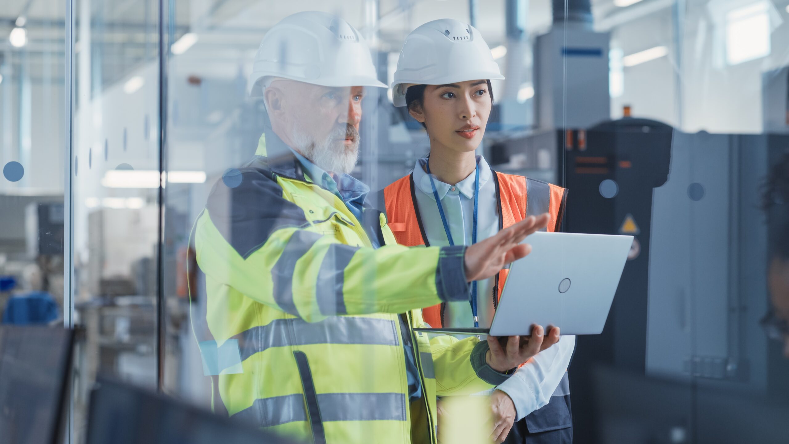 A male and female engineer in high vis and hard hats looking at laptop in a manufacturing setting