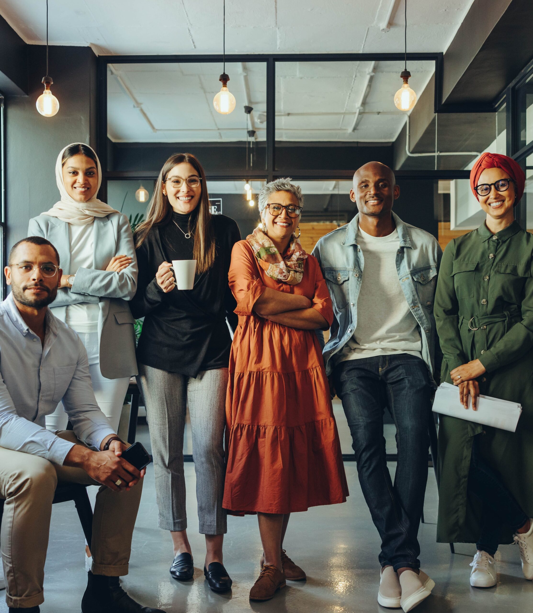 A diverse group of six professionals in a modern office, dressed in smart-casual attire, posing confidently with a warm, stylish background.